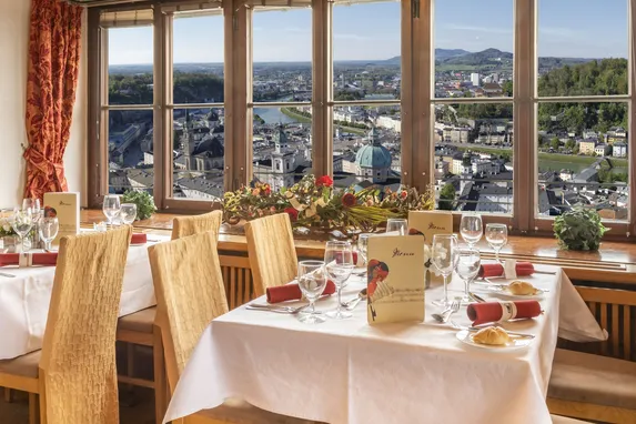 Elegante Restauranttische an Panoramafenster mit Blick auf Salzburgs Stadtlandschaft